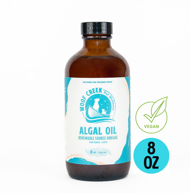 Glass bottle of Woof Creek Pet Wellness Algal Omega-3 plant-based oil for dogs and cats, 8 fl oz, with a label showing algae illustration.