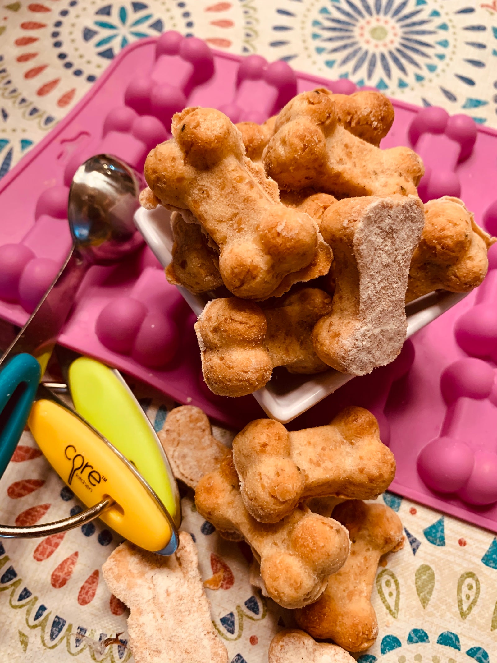 Home baked dog bone shaped cookies with pink bone mold and colorful measuring spoons. 